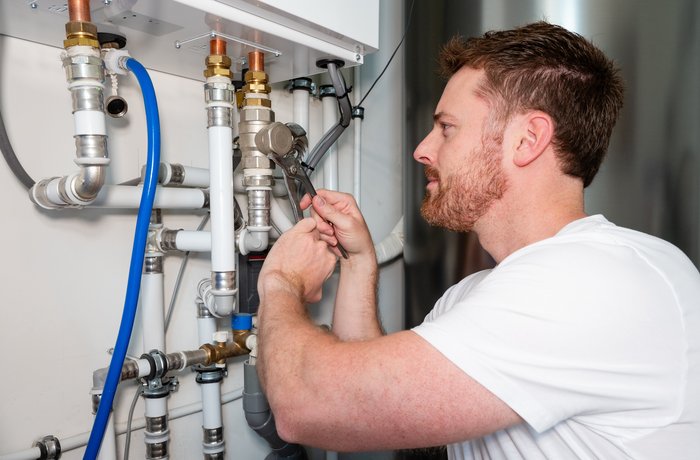 Ein Mann schraubt ein Heizungsrohr an einer neuen Wärmepumpe an