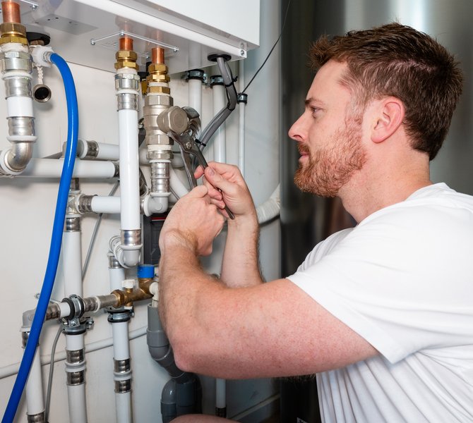 Ein Mann schraubt ein Heizungsrohr an einer neuen Wärmepumpe an