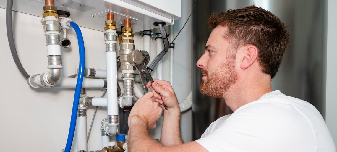 Ein Mann schraubt ein Heizungsrohr an einer neuen Wärmepumpe an