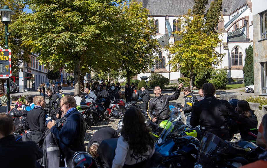 Große Gruppe von Motorrädern und -Fahrern auf dem Dorfplatz