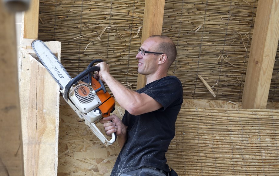 Ein Mann im T-Shirt schneidet einen Holzbalken mit der Kettensäge