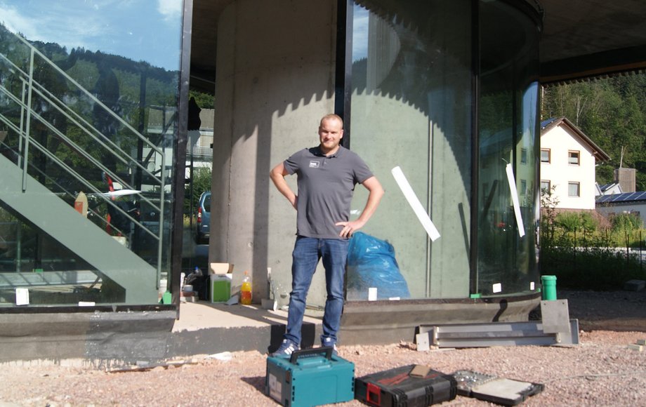 Mann steht mit Werkzeugkasten vor Glasfassade