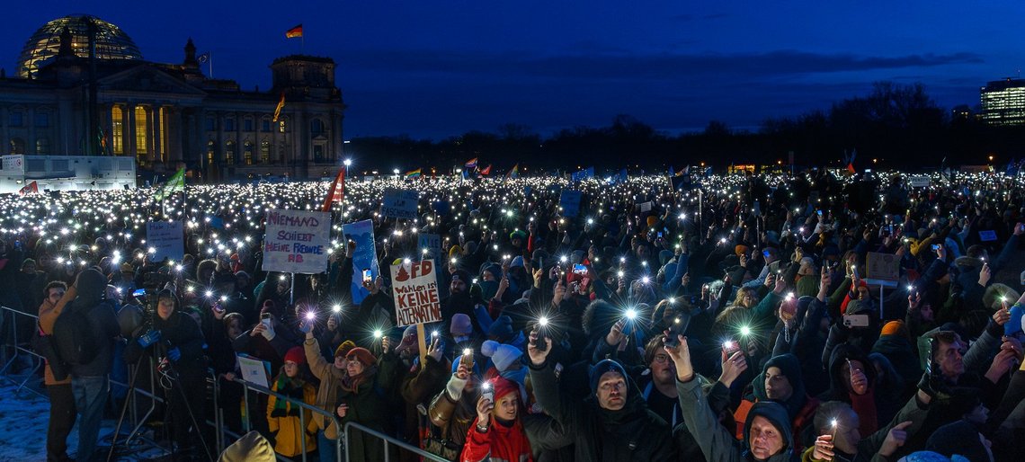 Große Menschenmenge vor Berliner Reichstag, die bei Nacht Taschenlampen leuchten lasen