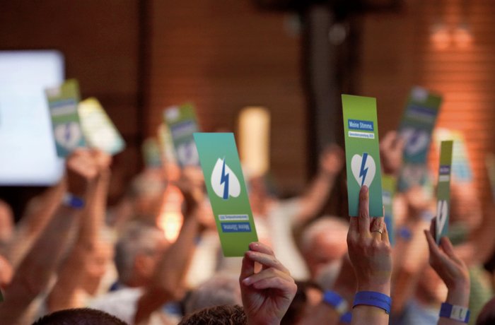 Menschen halten auf einer Versammlung Stimmkarten in die Höhe