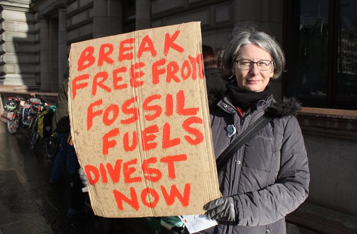 Frau hält Schild hoch: Break free from fossil fuels, divest now