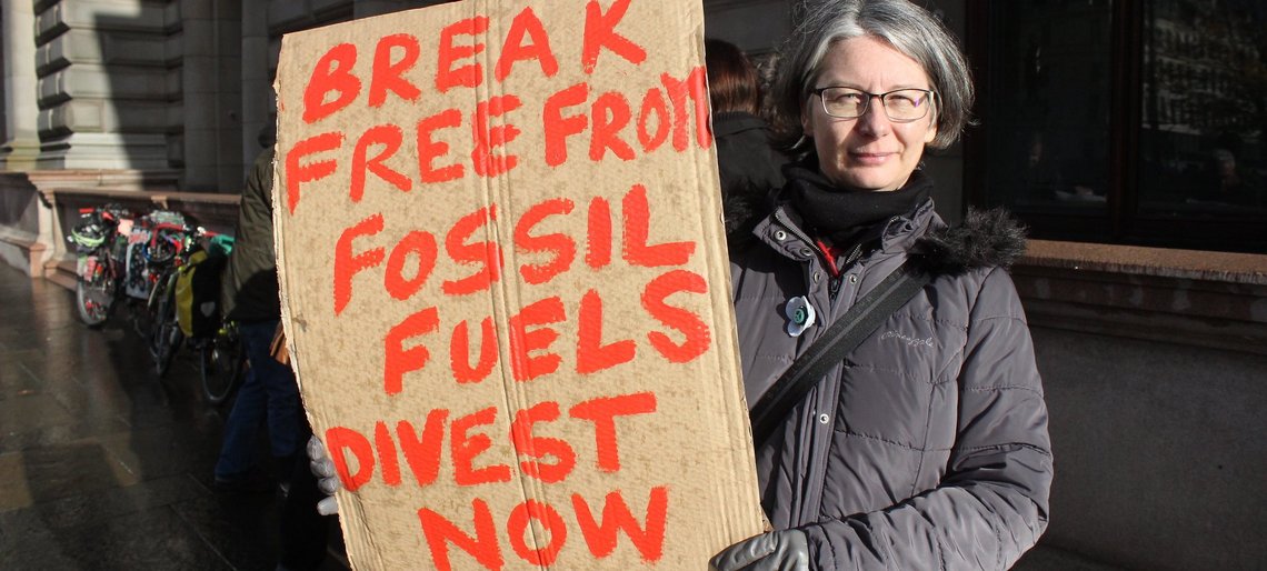 Frau hält Schild hoch: Break free from fossil fuels, divest now