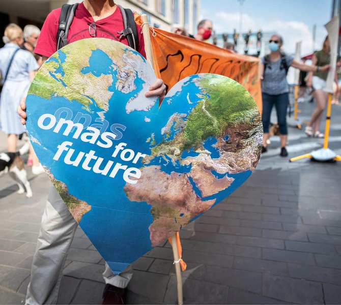 Eine ältere Frau hält ein Schild mit dem Erdherz, das Logo der Omas For Future, hoch