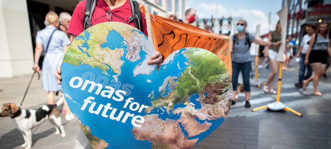 Eine ältere Frau hält ein Schild mit dem Erdherz, das Logo der Omas For Future, hoch