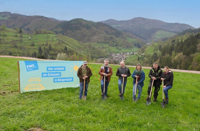 Fünf Menschen mit Spaten stehen neben großem Banner an einem grünen Hügel