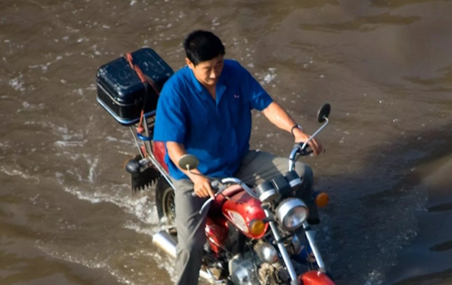 Mann in China fährt mit Mofa durch Hochwasser