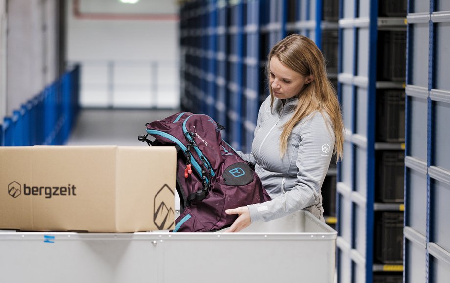 Mitarbeiterin packt einen Rucksack aus einem Karton