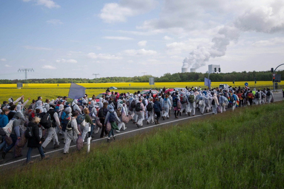 Dutzende von Aktivisten blockieren auf ihrem Marsch eine Landstraße, am Horizont sind die Kühltürme eines Kraftwerks zu sehen.