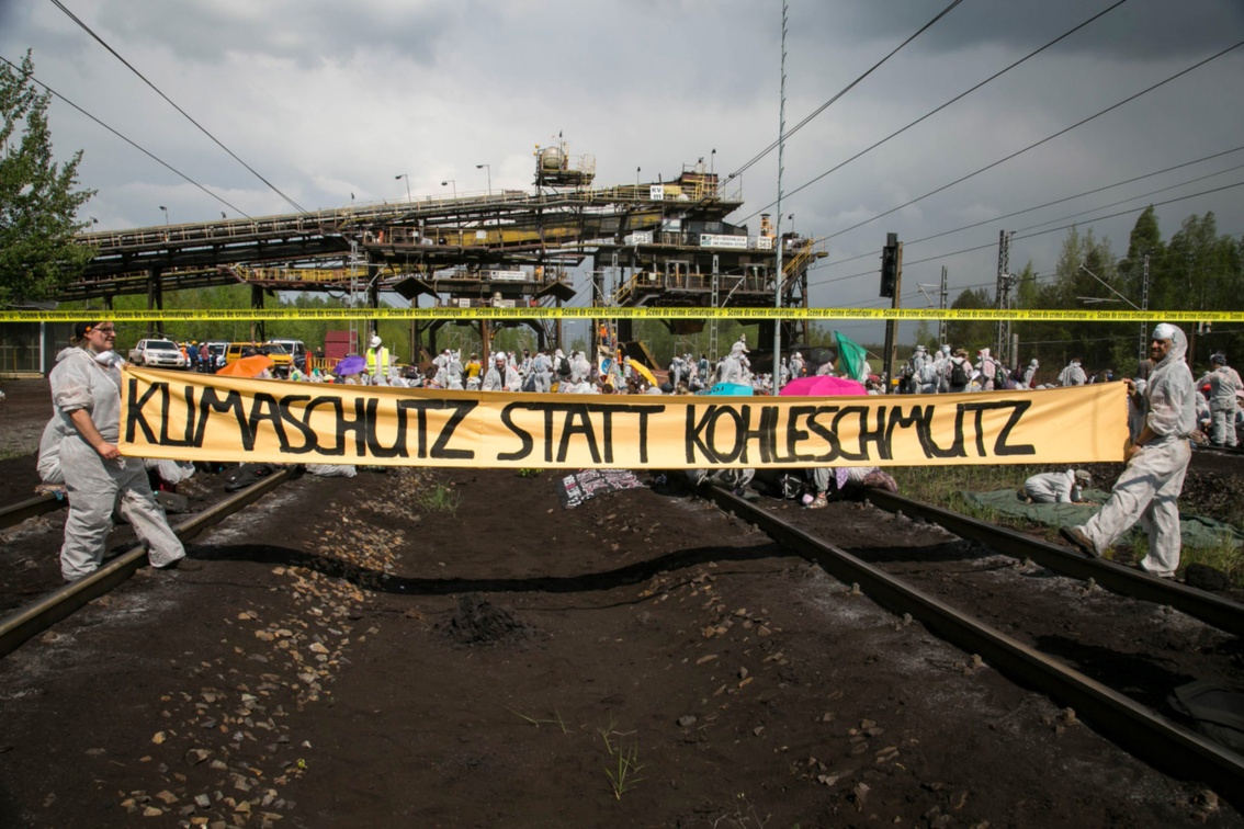 Aktivisten spannen ein Banner mit dem Schriftzug «Klimaschutz statt Kohleschmutz» quer über die Gleise zu einem Verladekran.