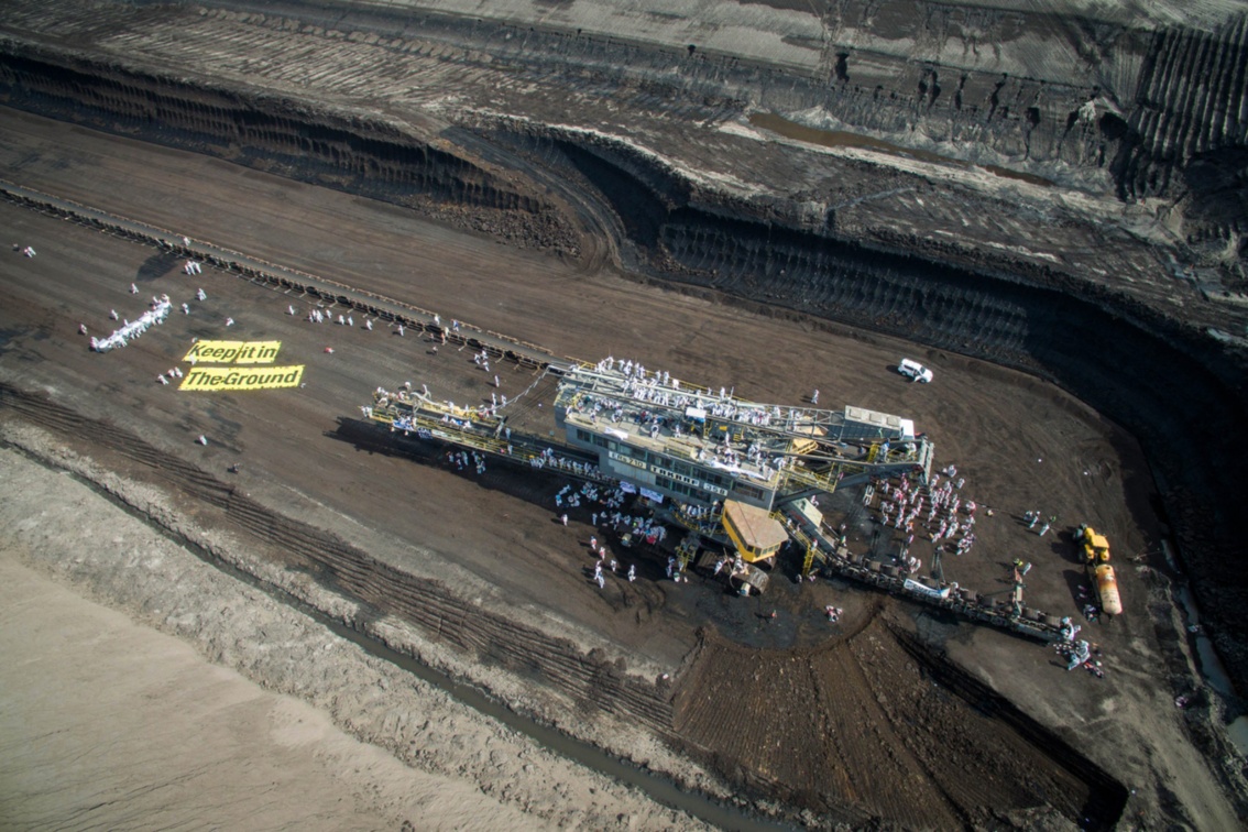 Luftbildaufnahme des besetzten Kohlebaggers, auf dem Boden daneben riesige Fahnen mit dem Schriftzug «Keep it in the ground!»