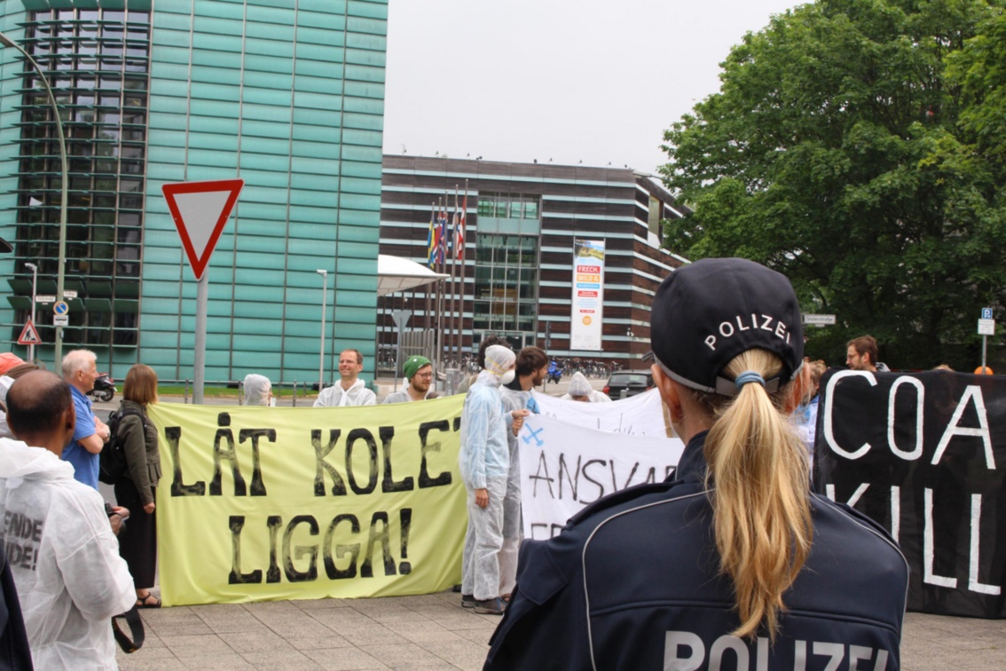 Eine Polizistin beobachtet Aktivisten, deren Banner mit schwedischen Anti-Kohle-Slogans beschriftet sind.