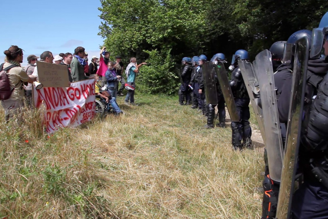 Demonstranten und Polizisten in Schutzausrüstung stehen sich am Waldrand direkt gegenüber.
