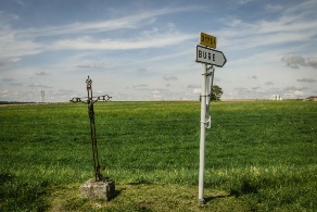 Ein Wegkreuz neben einem Schild, das zur französischen Gemeinde Bure weist.