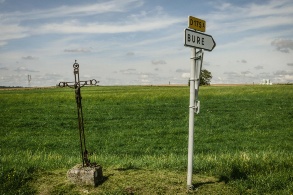 Ein Wegkreuz neben Schild, dass in die französische Gemeinde Bure weist.
