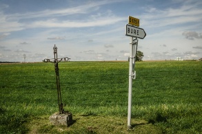 Ein Wegkreuz neben Schild, dass in die französische Gemeinde Bure weist.