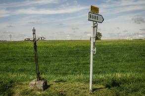 Ein Flurkreuz neben einem Schild, das zur französischen Gemeinde Bure weist.