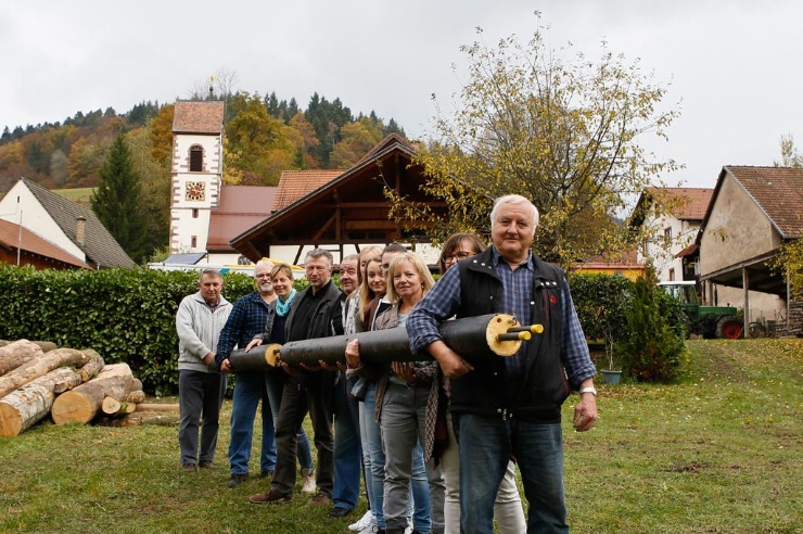 Elf Menschen posieren mit einem Nahwärmerohr auf einer Dorfwiese.