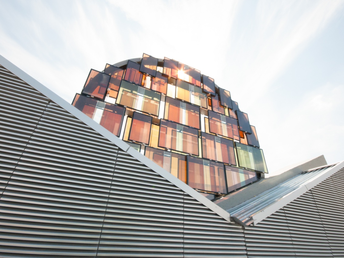 Futuristisch anmutendes Gebäude; vor der bogenförmigen Fassade sind rechteckige Energieglaselemente montiert.