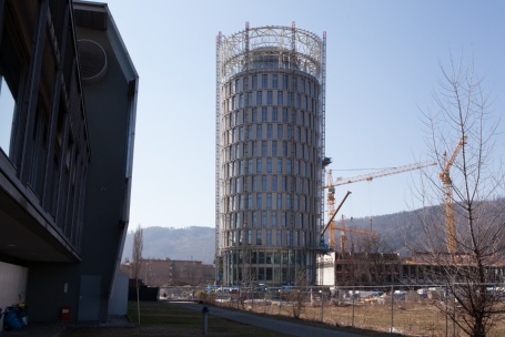 Ein zylindrischer, von einem Gerüst umgebener Turmbau, daneben drei Baukräne