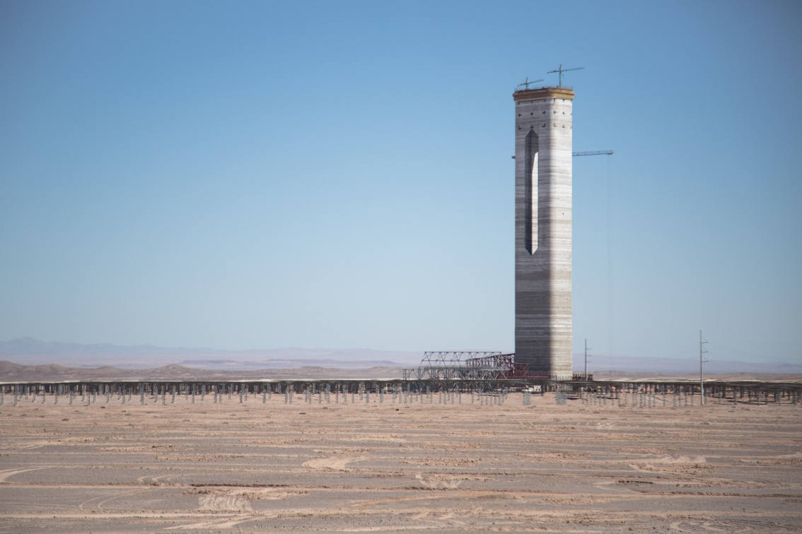 Inmitten einer Wüstenlandschaft ragt ein riesiger im Rohbau befindlicher Turm auf, dessen obere Hälfte schlitzartig durchbrochen ist.