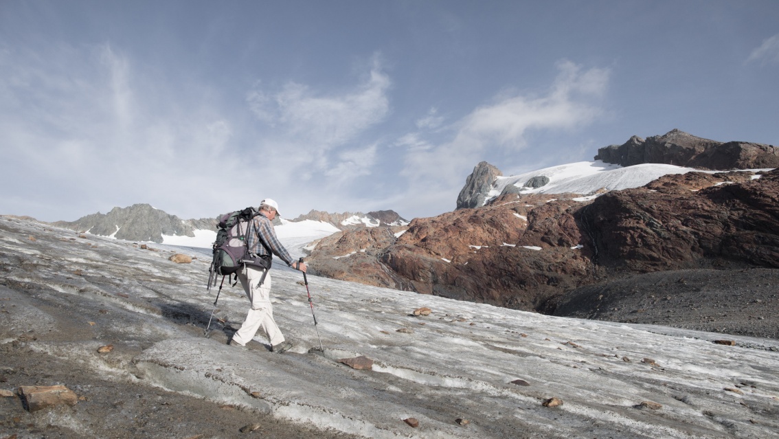 Ludwig Braun läuft in Wandermontur über einen mit Eisresten und einigen Steinbrocken überzogenen, leicht abschüssigen Hang.