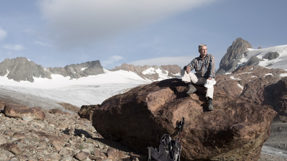 Ludwig Braun sitzt in Wanderkleidung auf einem Felsblock am Gletscherrand.