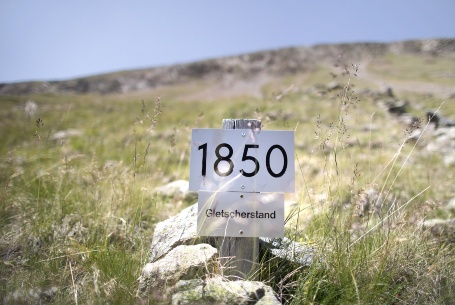 Ein Schild auf einer Bergwiese zeigt die Jahreszahl 1850 und und Aufschrift «Gletscherstand».