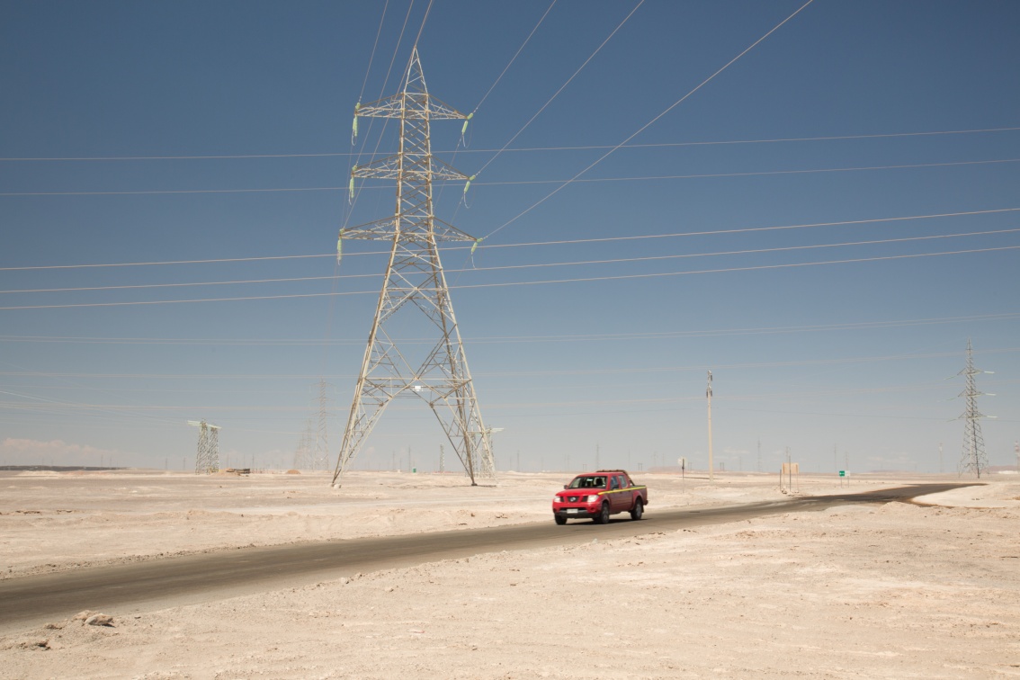 In der Wüstenlandschaft fährt ein roter SUV unter einer Stromleitung hindurch.