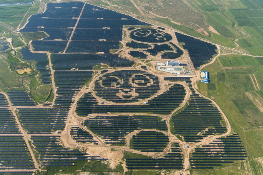 Luftbild eines riesigen Solarparks: Die hellen Wege zwischen den dunklen PV-Modulen bilden die Umrisse zweier Pandas ab..