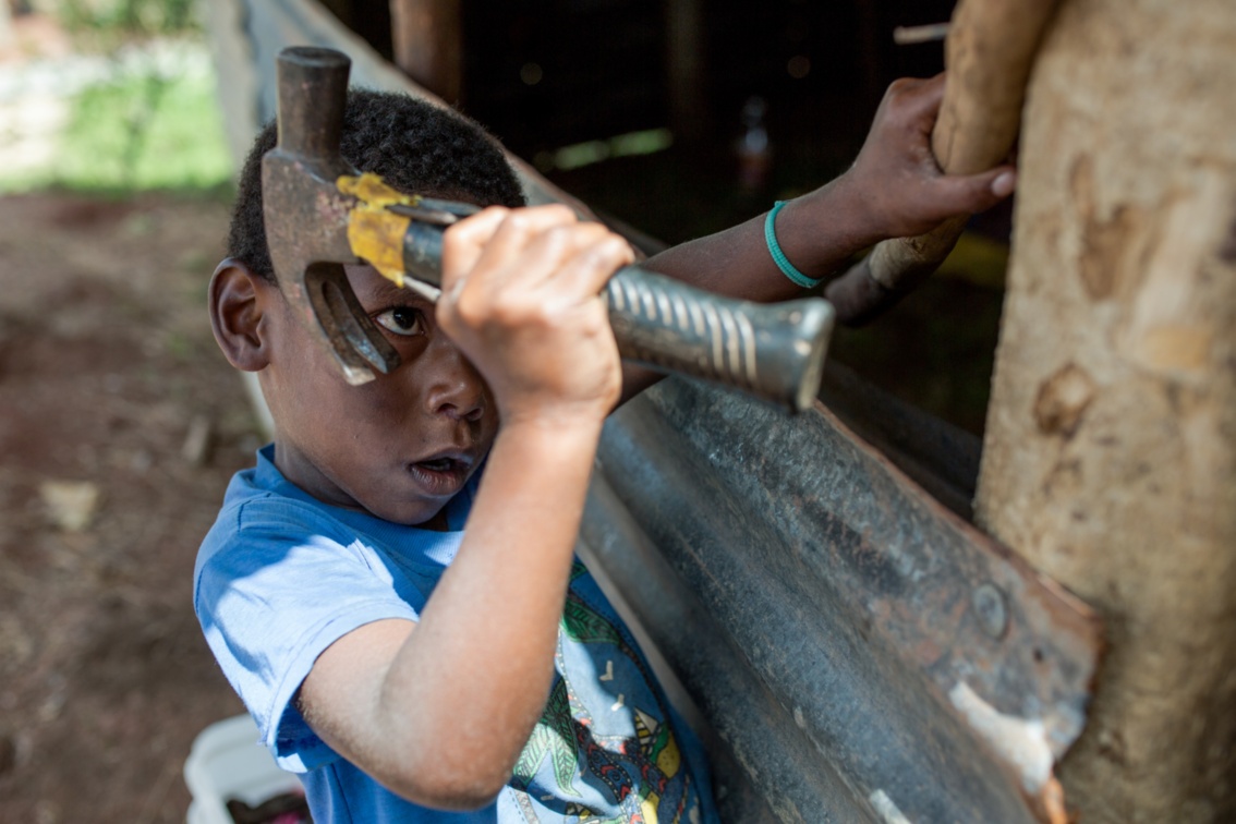 Ein kleiner Junge hilft mit einem großen Hammer bei Hausbau.