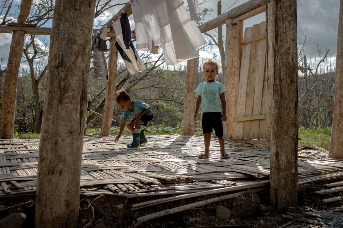 Zwei Kinder stehen in einem zerstörten Haus von dem nur noch ein Pfeiler und die Tür stehen.