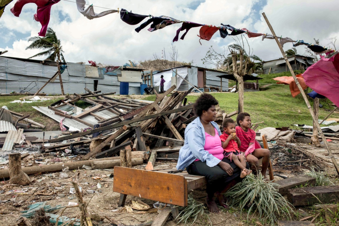 Eine Mutter sitzt mit Kindern auf einem Bettgestell in den Trümmern ihres Hauses.