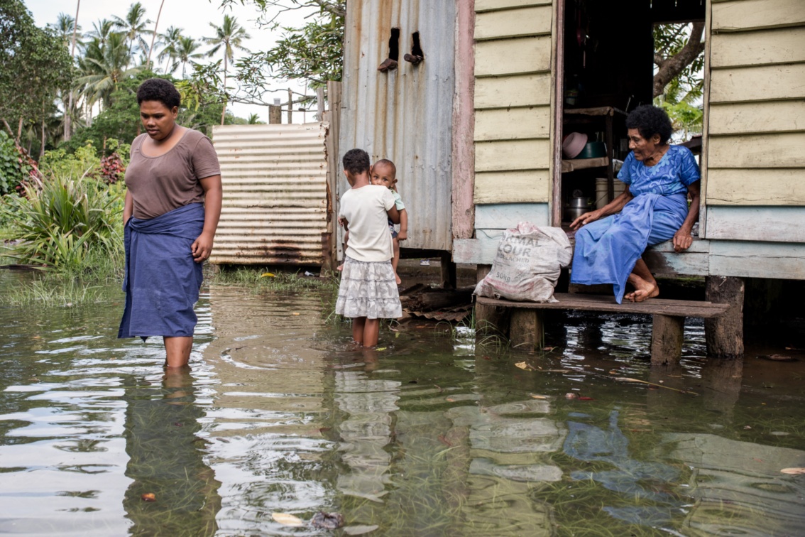 Familie Dirit steht im Wasser vor ihrem Haus auf Stelzen