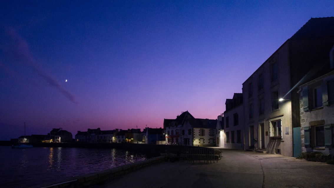 Violett-blauer Abendhimmel und Licht der Straßenlaternen über der Häuserzeile am Hafen.