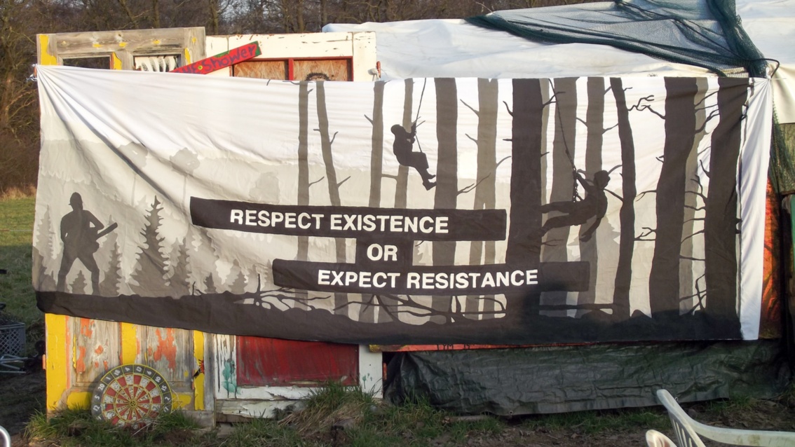 Auf einem Banner sind Bäume abgebildet, darauf steht der Text: «Respect existence or expect resistance»