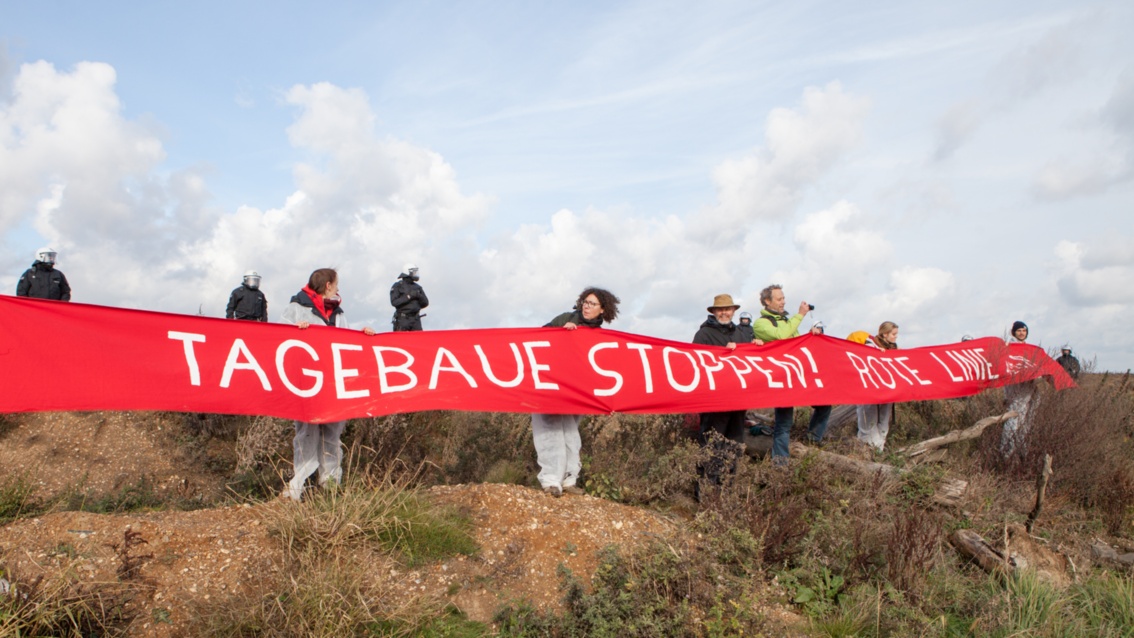 Etwa 10 Demonstrationen halten ein langes rotes Banner mit der Aufschrift «Tagebaue stoppen, Rote Linie»