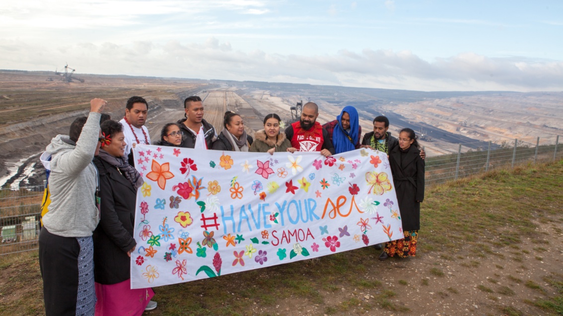 Die Gruppe posiert vor der Kante des Tagebaugeländes mit dem bunt bemalten Banner. 