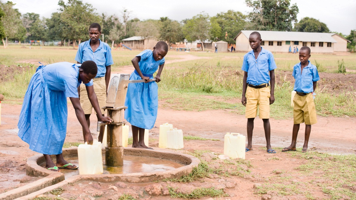 Fünf Kinder stehen am Brunnen und zapfen Wasser.