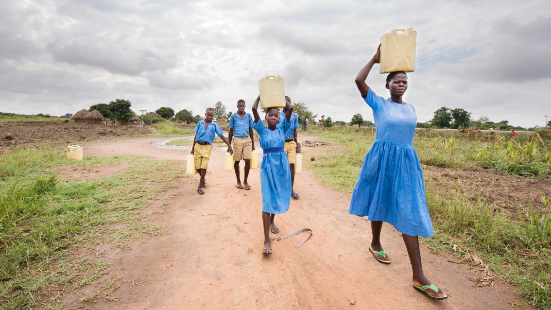 Eine Gruppe Kinder tragen Wasser in Kanistern auf dem Kopf.