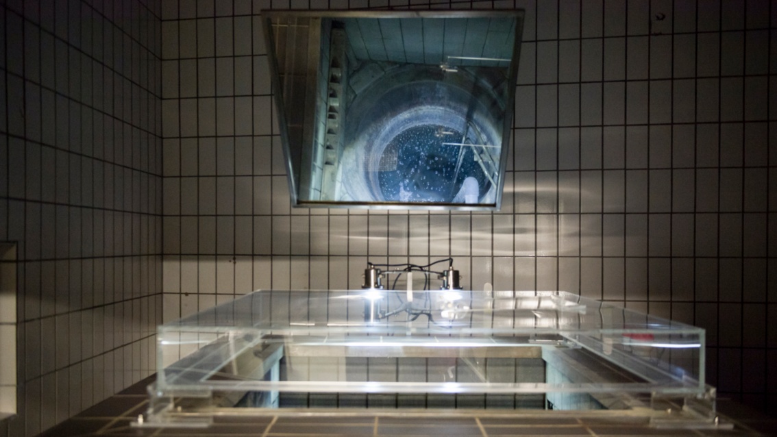 Durch einen Spiegel sieht man in das Innere des gekachelten Brunnens, der mit Plexiglas abgedeckt ist