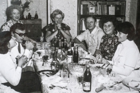 Ein zerkratztes Schwarzweißfoto zeigt eine fröhliche Geburtstagsgesellschaft am Tisch