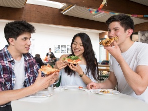 Drei ältere Schüler essen Pizza aus der Hand.