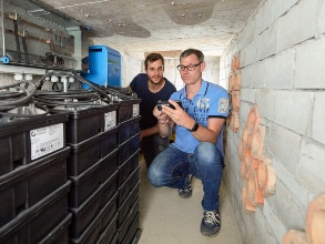 Zwei junge Männer in einem Keller an gestapelten schwarzen Salzwasserbatterien