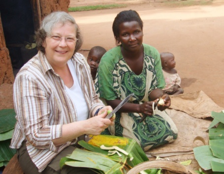 Bärbel Höhn sitzt gemeinsam mit einer ugandischen Mutter und zwei kleinen Kindern vor einem Haus und bereitet eine Mahlzeit vor.