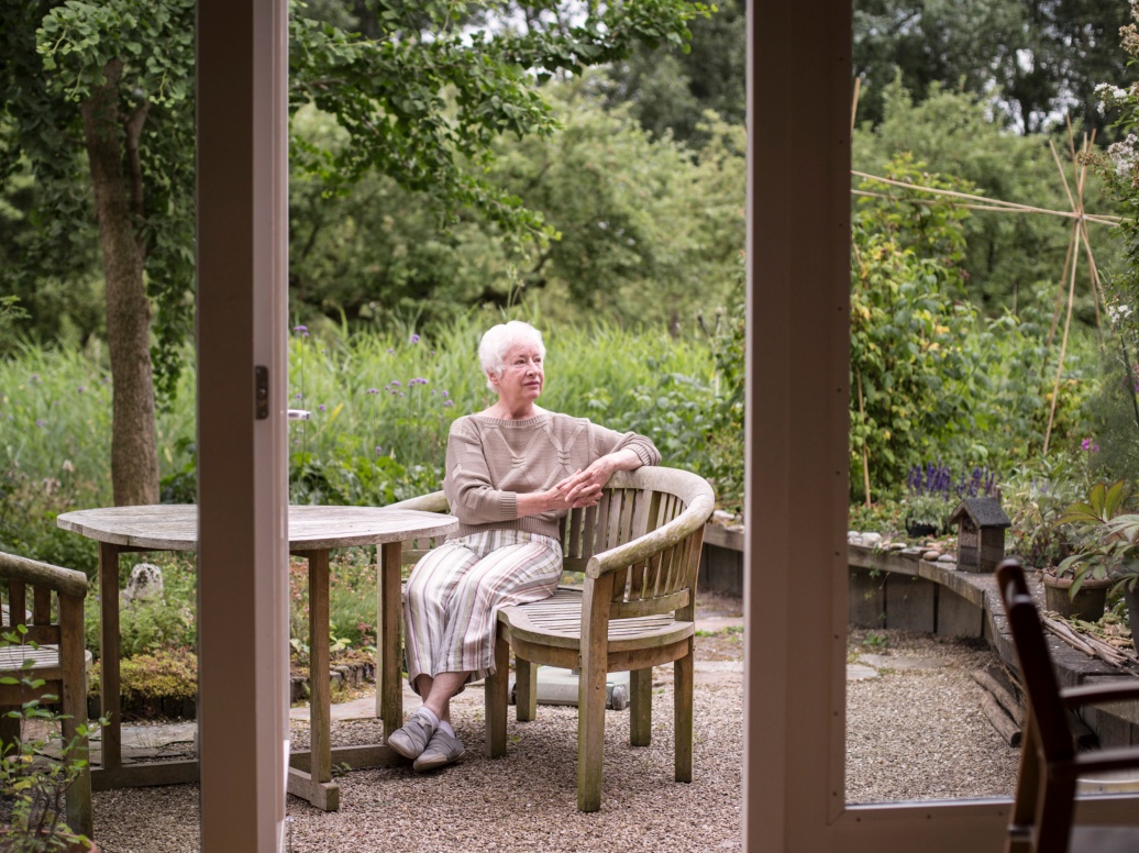 Eine ältere Dame mit kurzen grauen Haaren sitzt auf ihrer Terrasse.