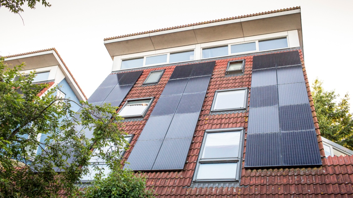 In drei Reihen sind Photovoltaik-Module an der steilen Dachfläche eines Wohnhauses montiert.